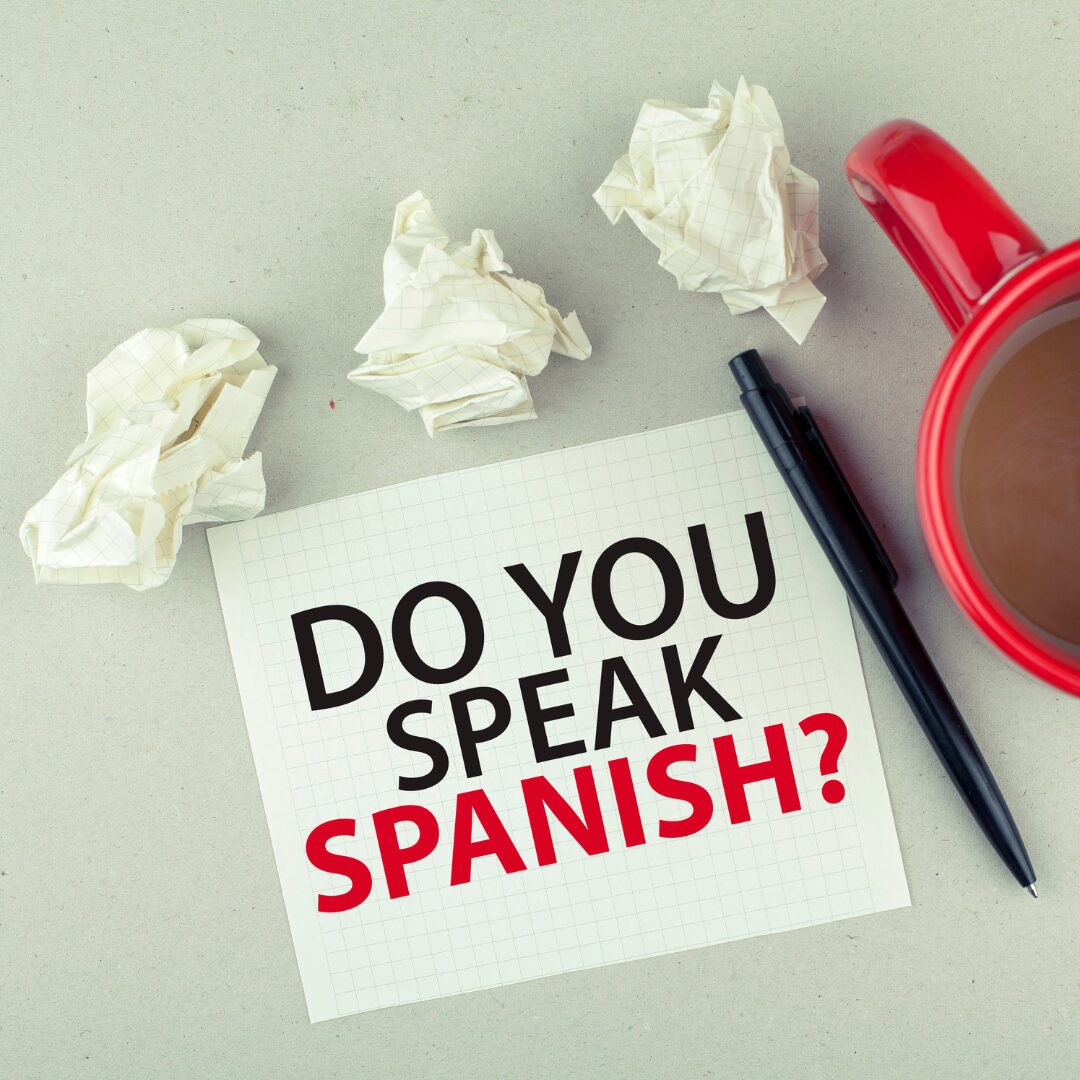 Nota en papel cuadriculado con el texto 'Do you speak Spanish?' acompañada de una taza de café, un bolígrafo y papeles arrugados