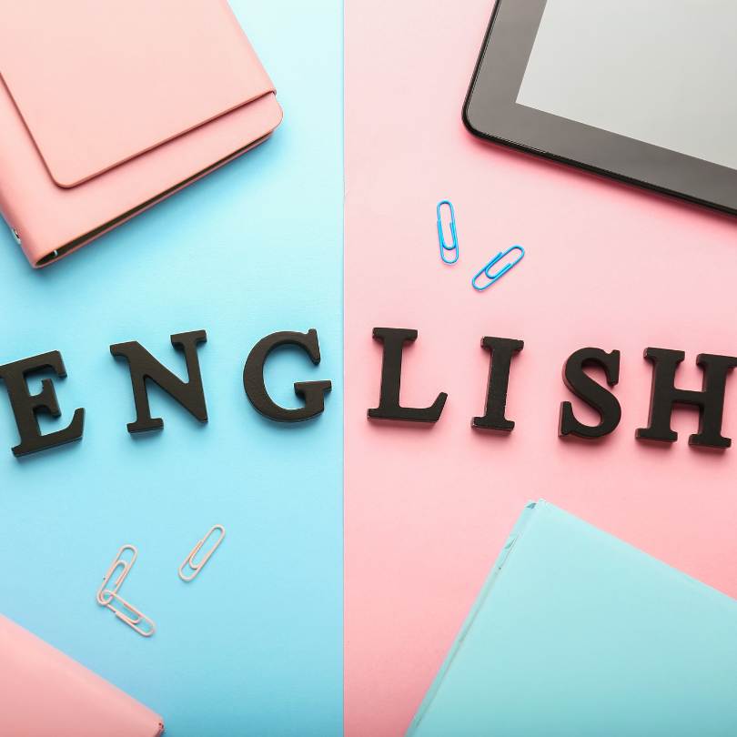 La palabra 'English' formada con letras negras sobre fondo dividido en azul y rosa, acompañada de útiles escolares y una tablet