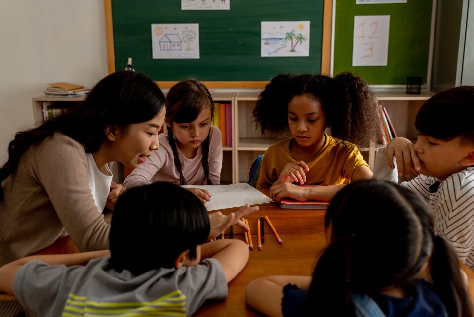 Profesora realizando una explicación con lápices a un grupo de alumnos