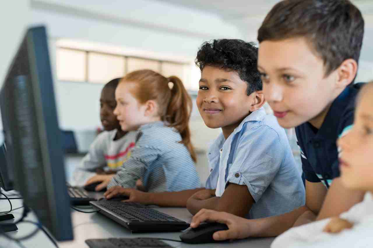 Grupo de niños de diversas etnias usando computadoras en un aula, participando en una actividad de aprendizaje digital