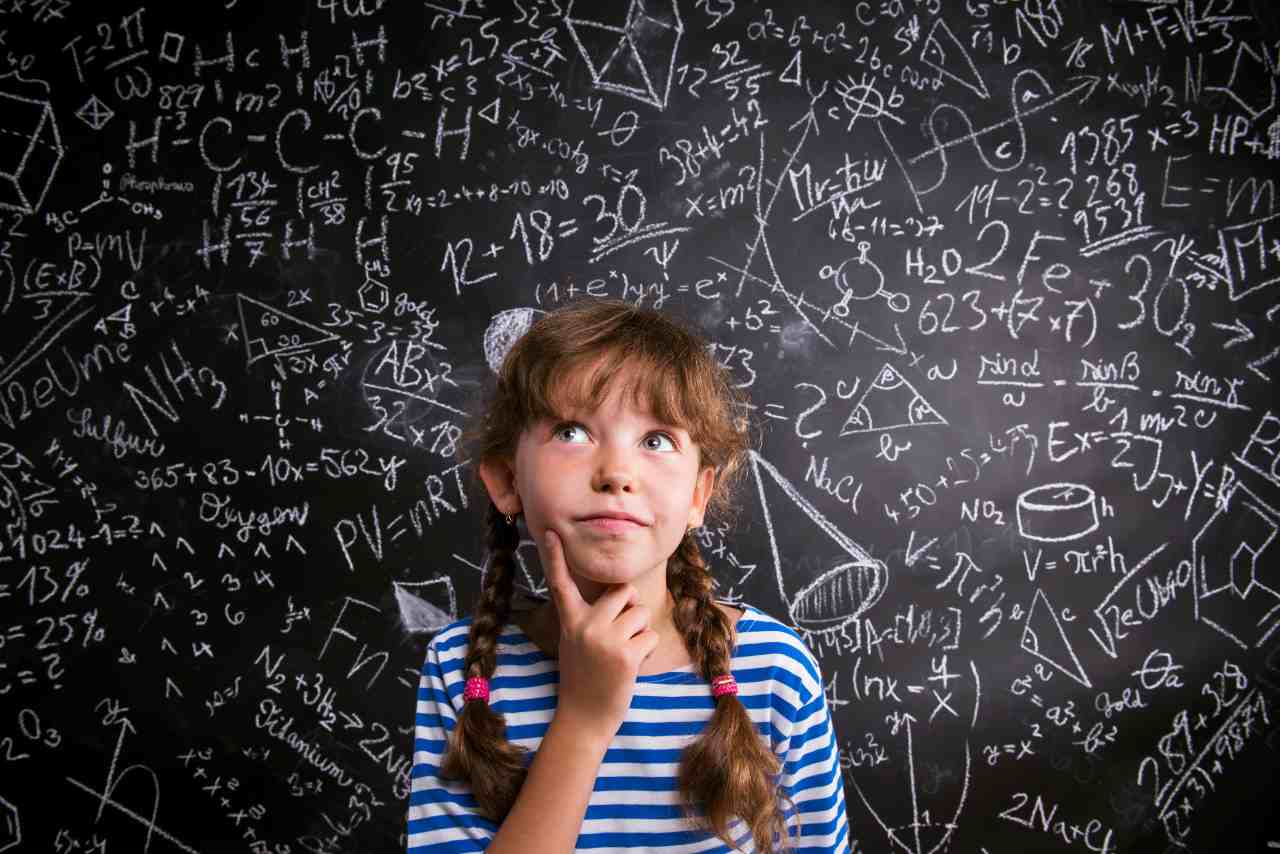 Niña pensativa frente a una pizarra llena de fórmulas matemáticas y científicas, representando curiosidad y aprendizaje en ciencia