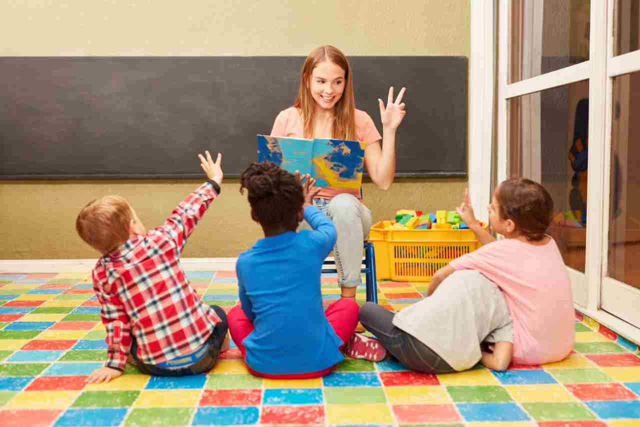 Maestra leyendo un cuento a un grupo de niños en un aula de preescolar, interactuando y haciendo preguntas mientras los niños participan