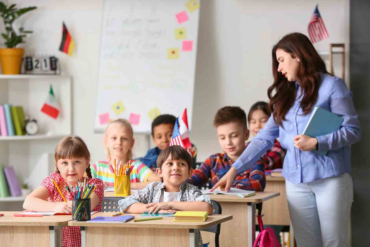 Maestra interactuando con un grupo diverso de niños en un aula decorada con banderas internacionales, promoviendo el aprendizaje multicultural