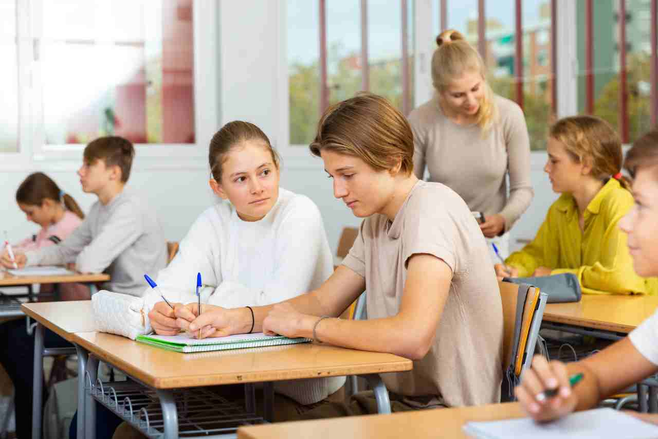 Estudiantes colaborando en una actividad en el aula mientras la profesora observa y guía a otros alumnos