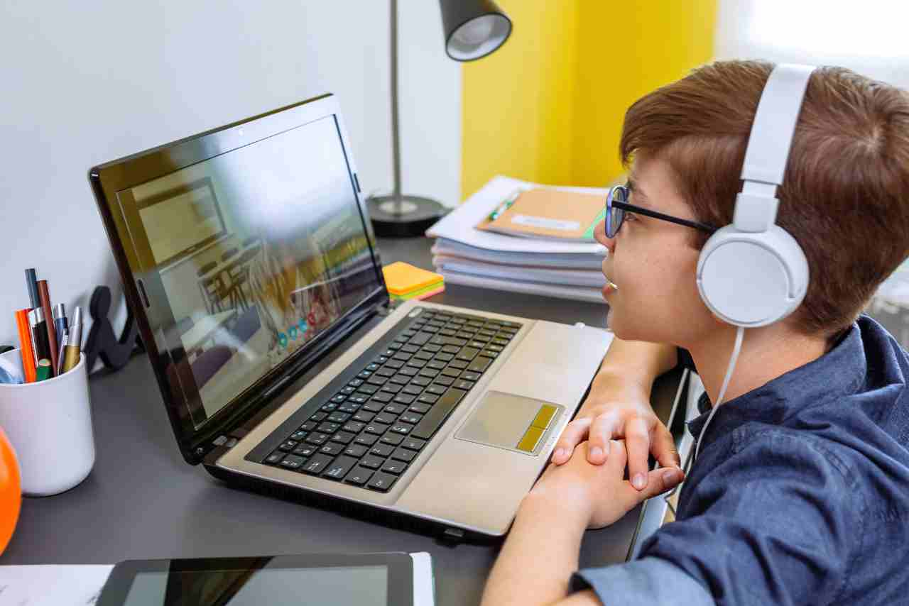 Niño con auriculares participando en una clase en línea desde su laptop en un escritorio, rodeado de materiales escolares