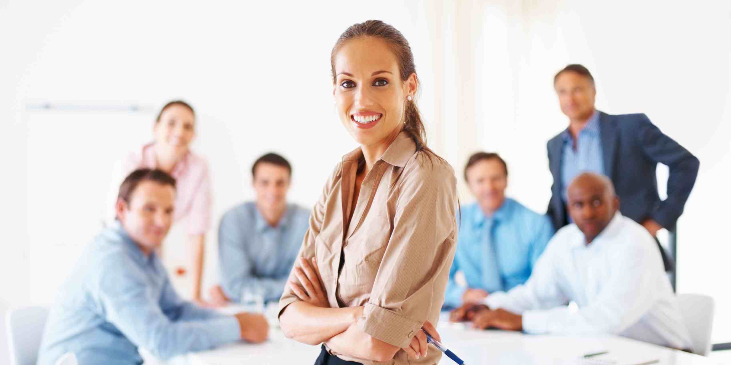 Mujer profesional sonriente en primer plano, rodeada de un equipo de colegas en una sala de reuniones